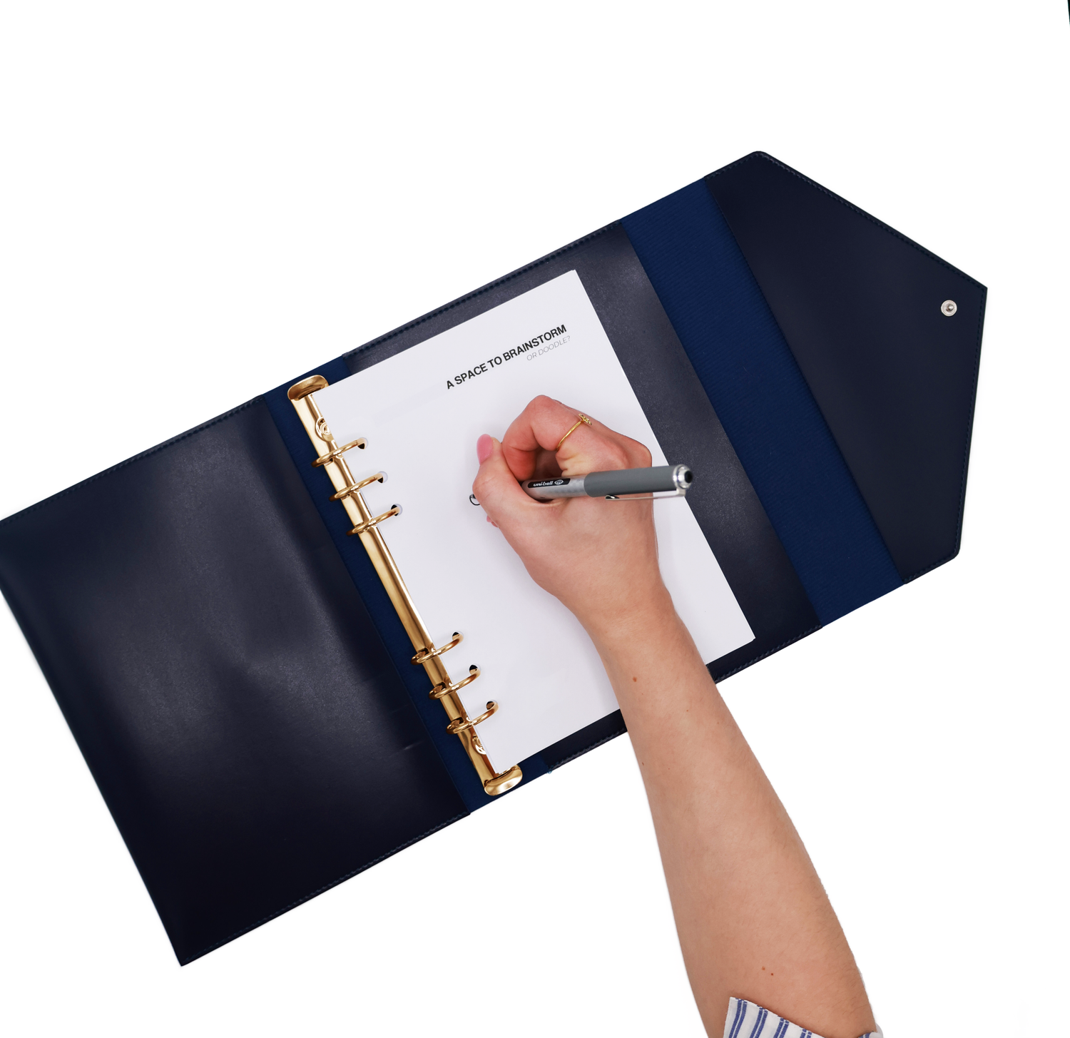 The Hummingbird Planner open from above with a hand writing on the insert page labelled 'a space to brainstorm', The image shows its refillable six-ring binding and clean planner inserts. The navy vegan leather A5 organiser features elegant gold hardware, ideal for personalised, customisable planning for professionals and creatives.