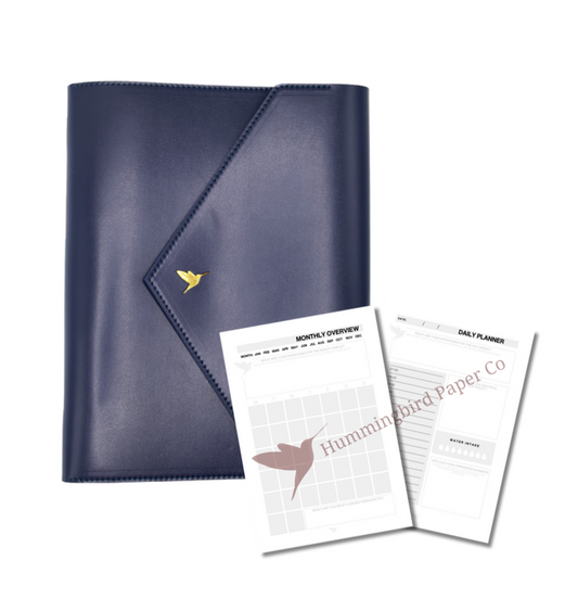 The Hummingbird Planner closed in navy vegan leather with gold foil hummingbird logo, shown alongside monthly and daily planner inserts. This personalised A5 refillable planner system is ideal for customisable organisation and productivity.